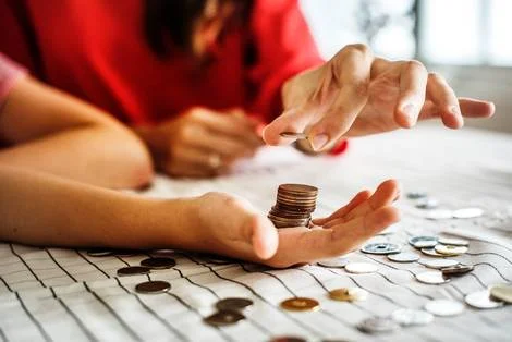 Hands holding a coin over a stack of coins.