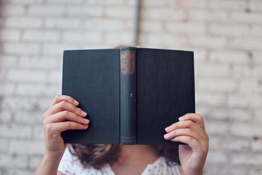 Girl holding book to cover her face.