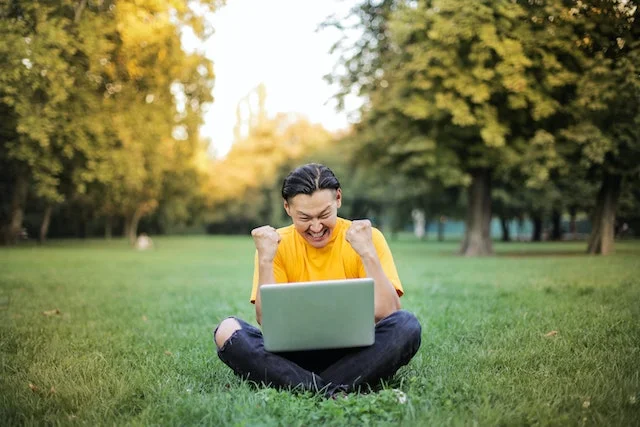 Male student looking at his laptop while cheering.